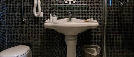 A bathroom with a pedestal sink, a toilet, a shower enclosure, and a mirror.