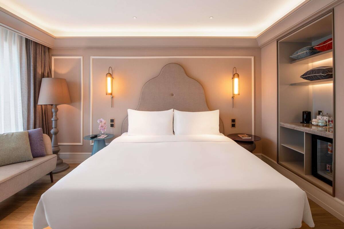 Ett hotellrum med en stor säng, sänglampor, ett nattduksbord, en soffa och en inbyggd garderob.