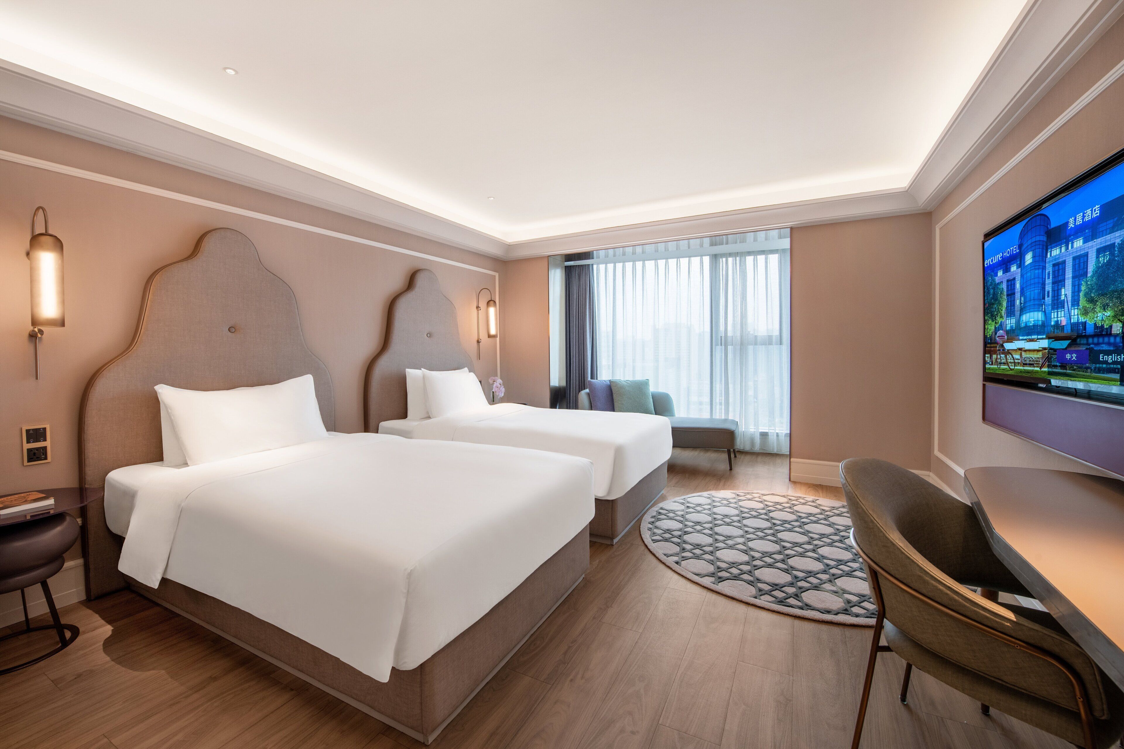 Habitación de hotel con dos camas, un escritorio, una silla, un televisor y un ventanal con cortinas.