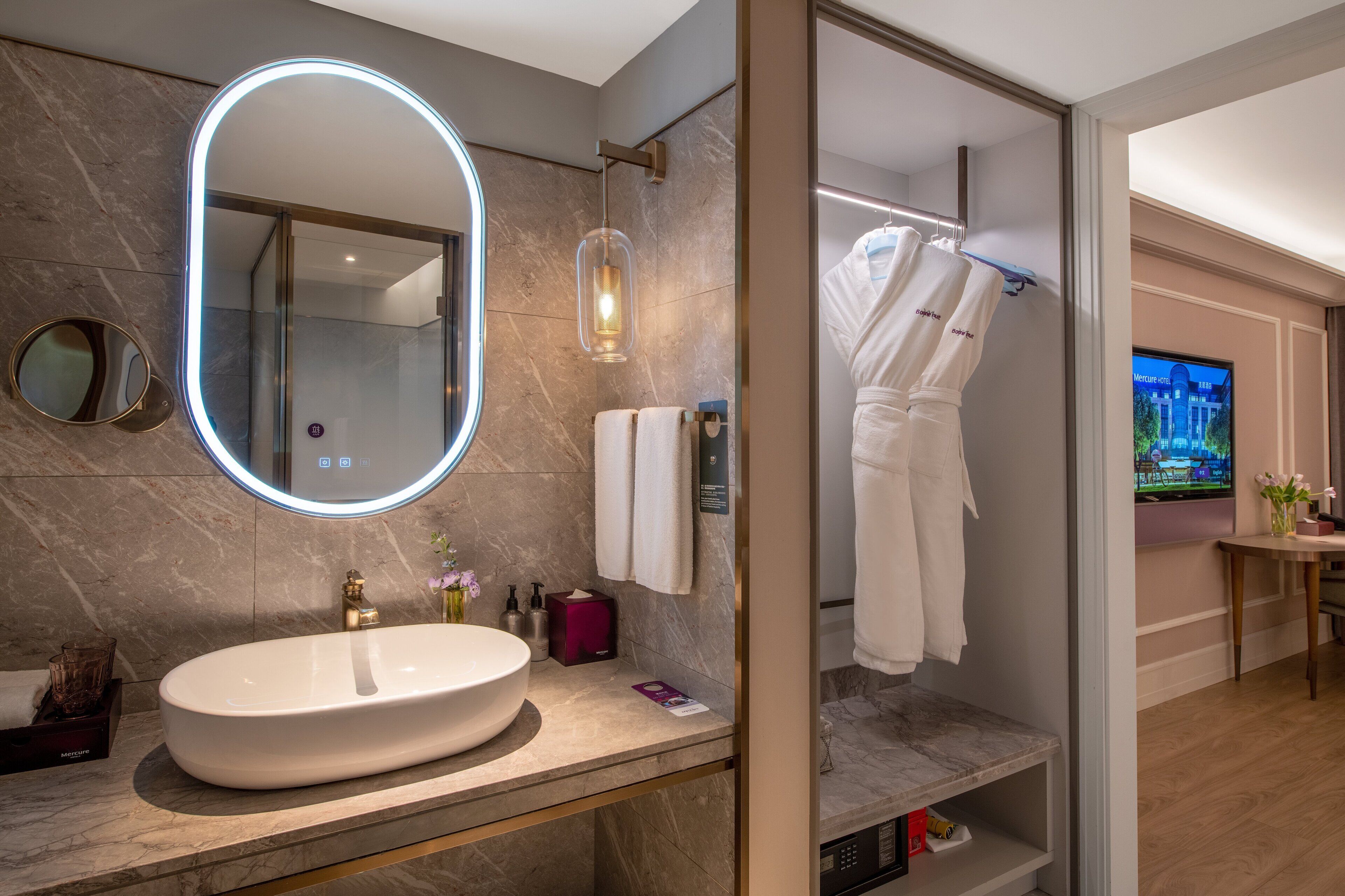 Un baño moderno con un lavamanos ovalado grande, un espejo con luz, zona de ducha y televisor.