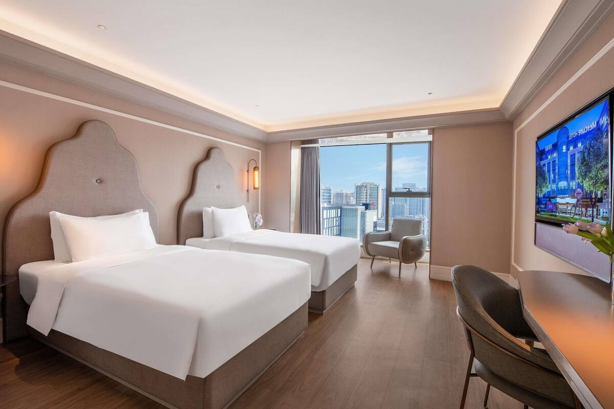 Ett hotellrum med två sängar, en TV, ett skrivbord och utsikt över staden.
