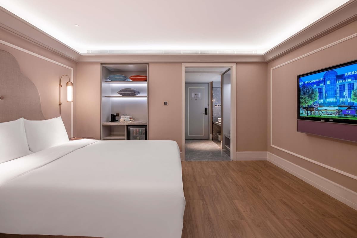 Ett hotellrum med en säng, en tv som är monterad på väggen, en inbyggd garderob och ett litet skrivbord.