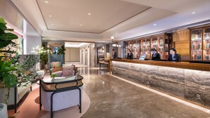 A modern hotel lobby with a marble reception desk, a seating area with a round table, and a bookshelf filled with books. - Mercure Chengdu Chunxi Taikoo Li (Chengdu)