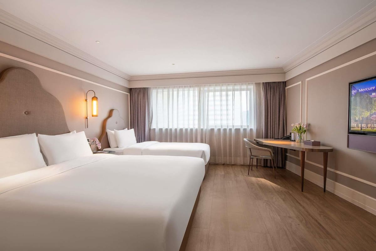 Habitación de hotel con dos camas, un escritorio, una silla, un televisor y una ventana con cortinas.
