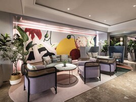 Un área de descanso moderna con asientos cómodos, un amplio mural abstracto y plantas en macetas.