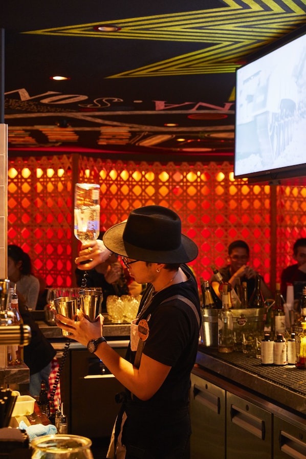 Un camarero en un bar con un muro estampado y una pantalla de televisión al fondo.