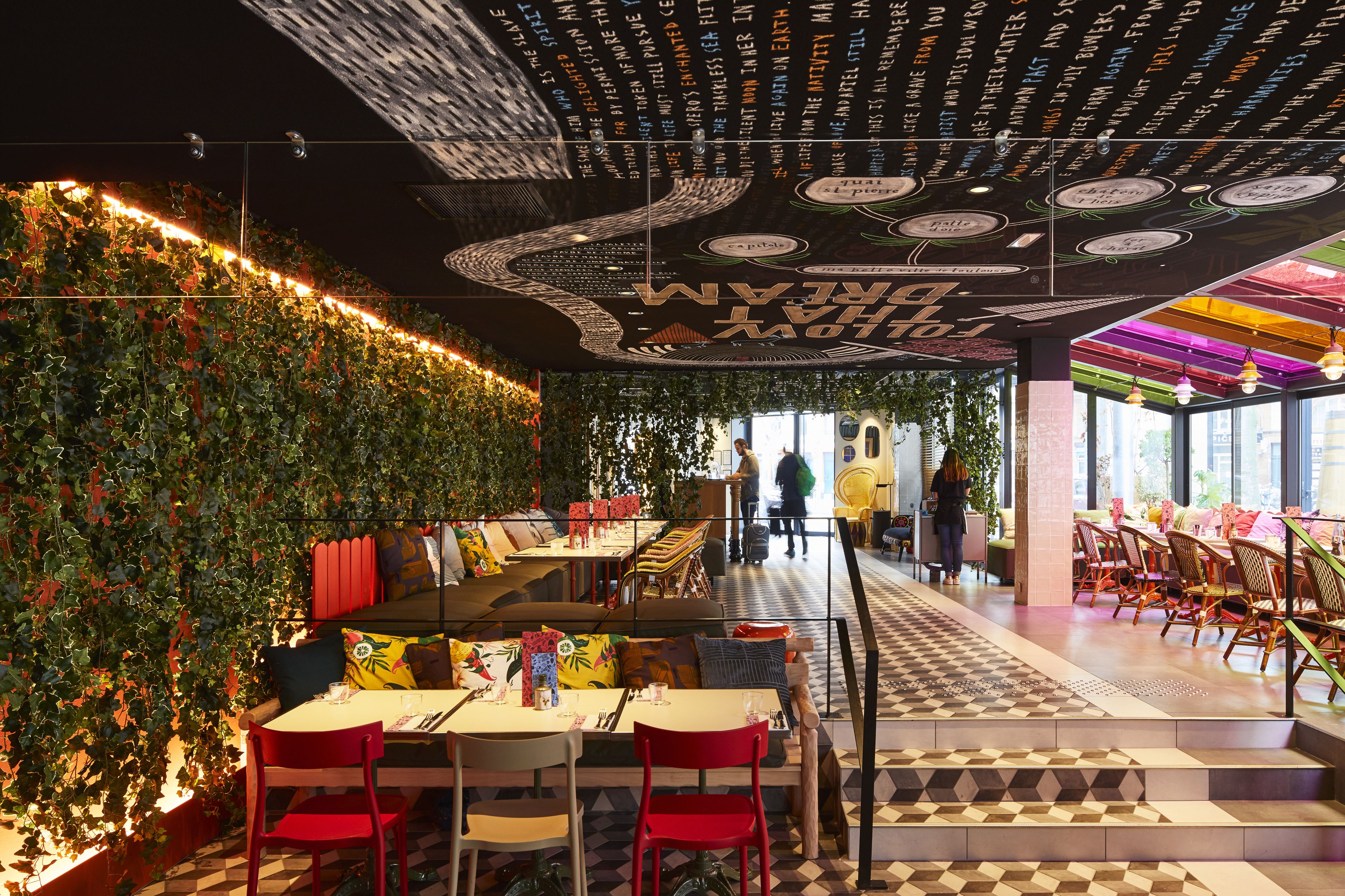 Un restaurant intérieur doté d’un mur végétal, d’un sol à carreaux et d’un plafond orné de motifs et d’inscriptions.