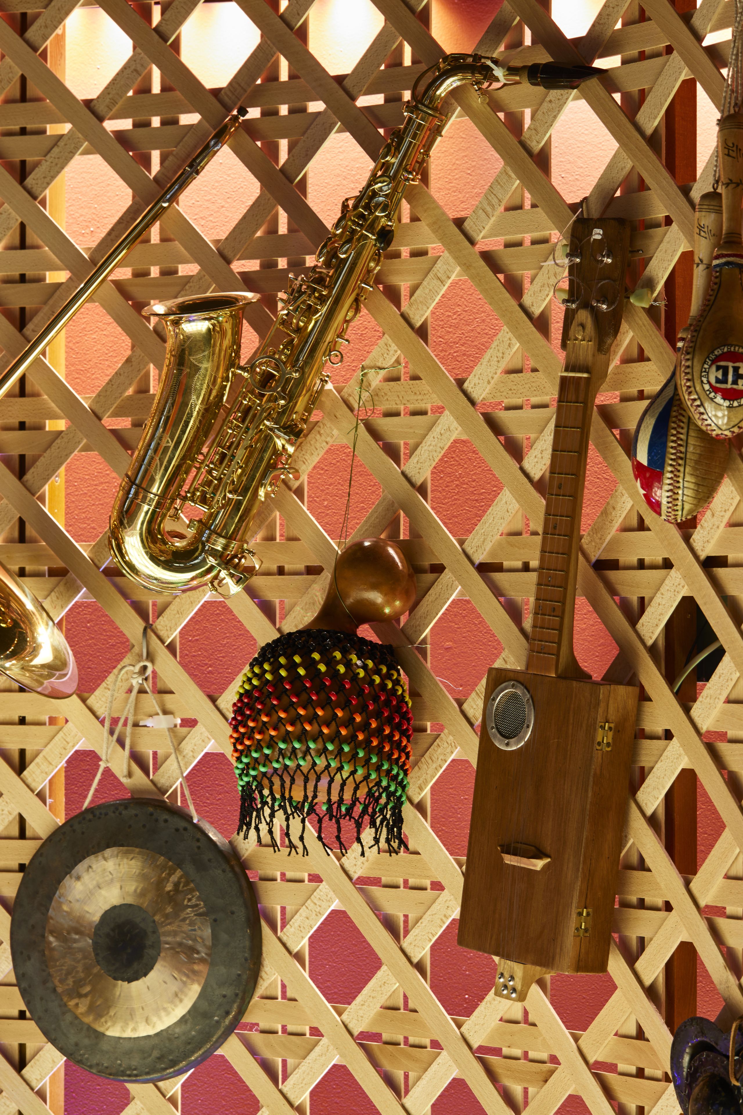 Un saxophone, une guitare, un tambourin et une batterie suspendus à un mur en treillis de bois.