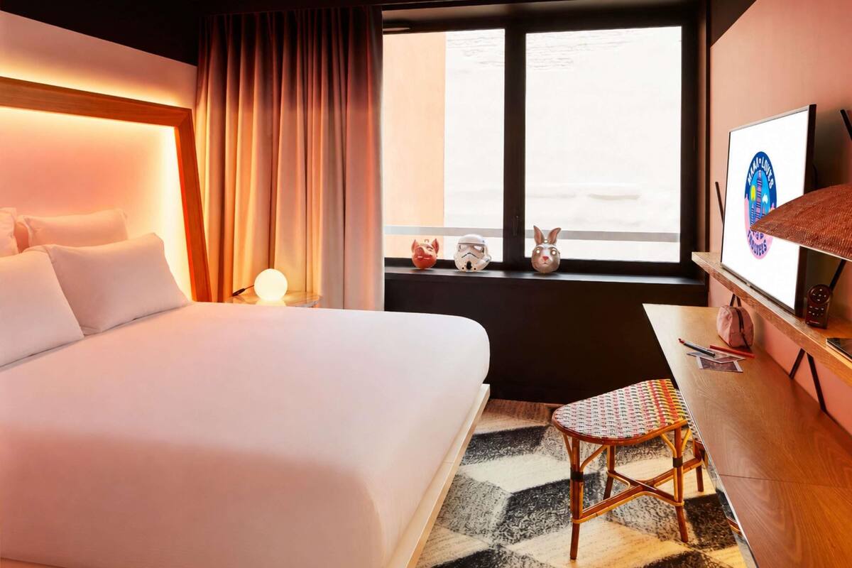 Una habitación de hotel con cama, escritorio, silla, televisión y ventana con cortinas.
