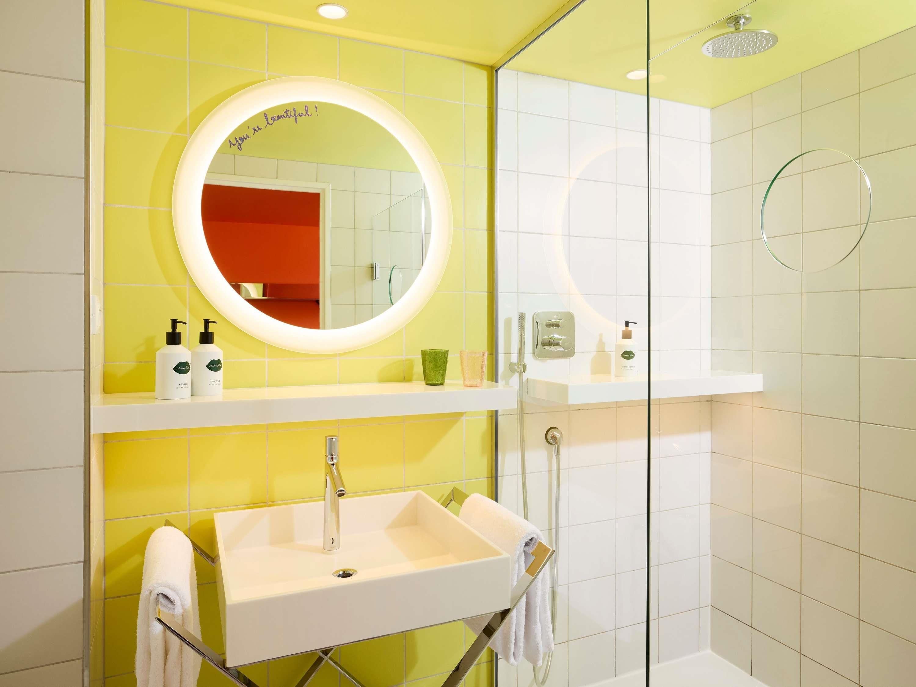 Une salle de bain avec un lavabo blanc, un miroir à cadre rond et une douche en verre.