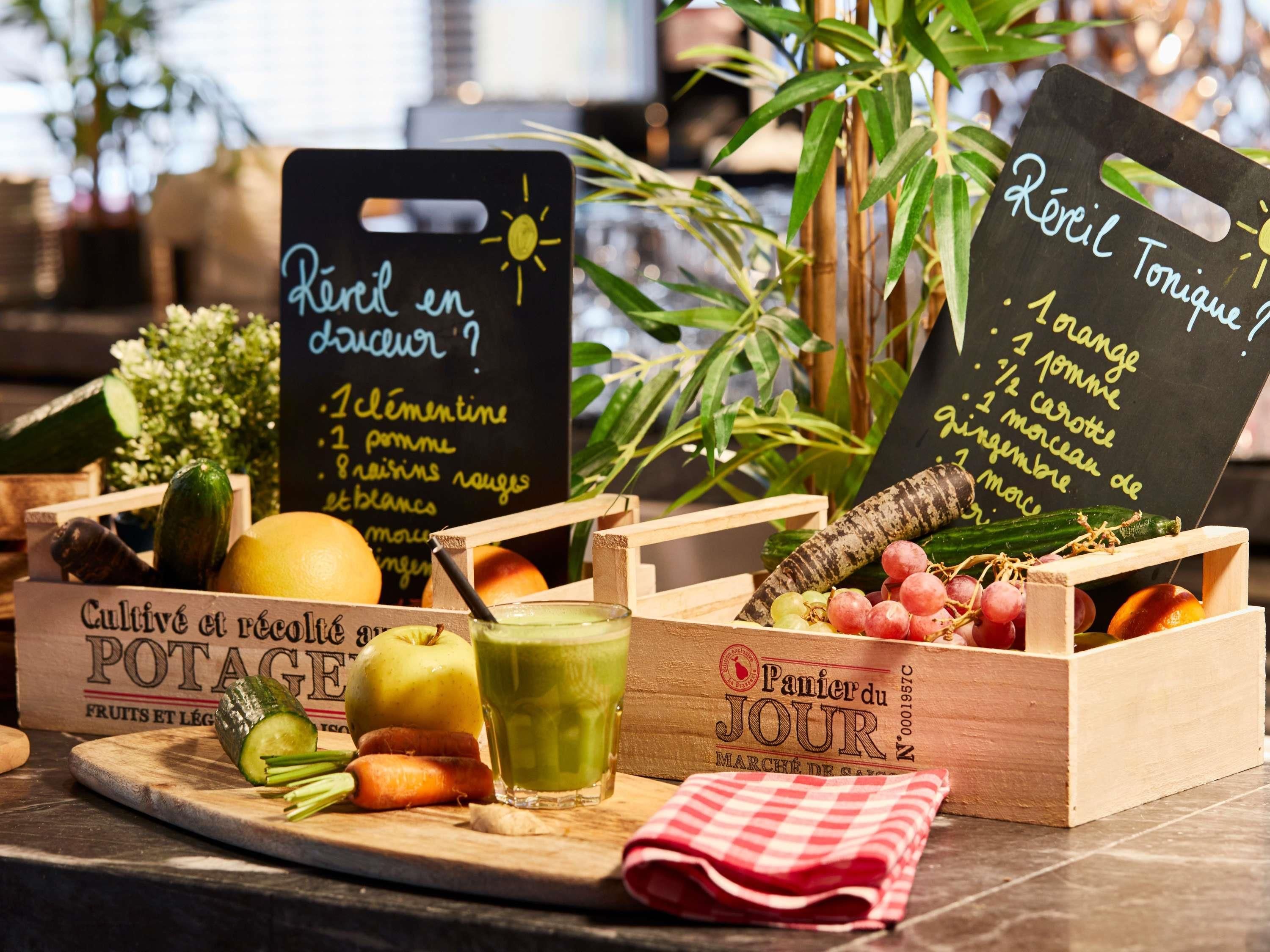 Eine Holzkiste mit einem grünen Smoothie, einer rot-weiß karierten Serviette und einer Kreidetafel mit Speisen wie Äpfeln, Karotten und Trauben.