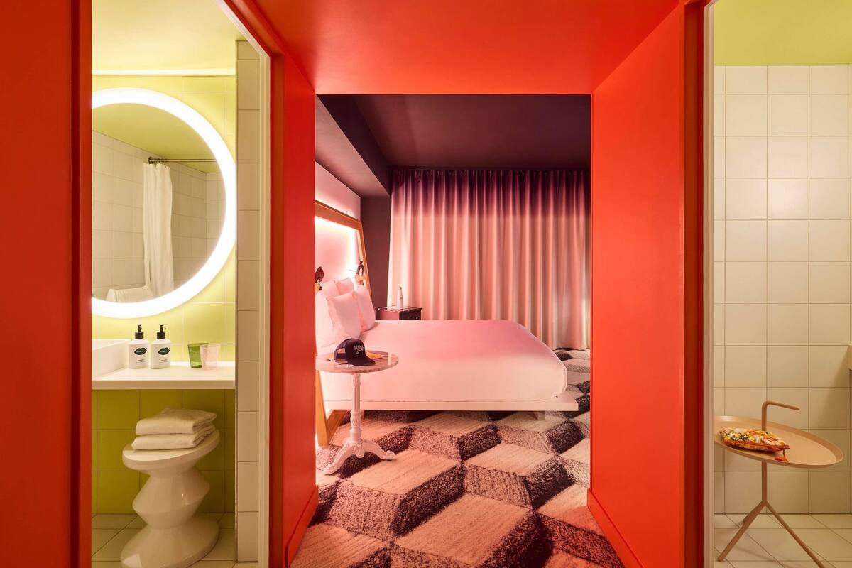 Una habitación de hotel moderna con cama, baño con espejo redondo y una pequeña mesa con una pizza.