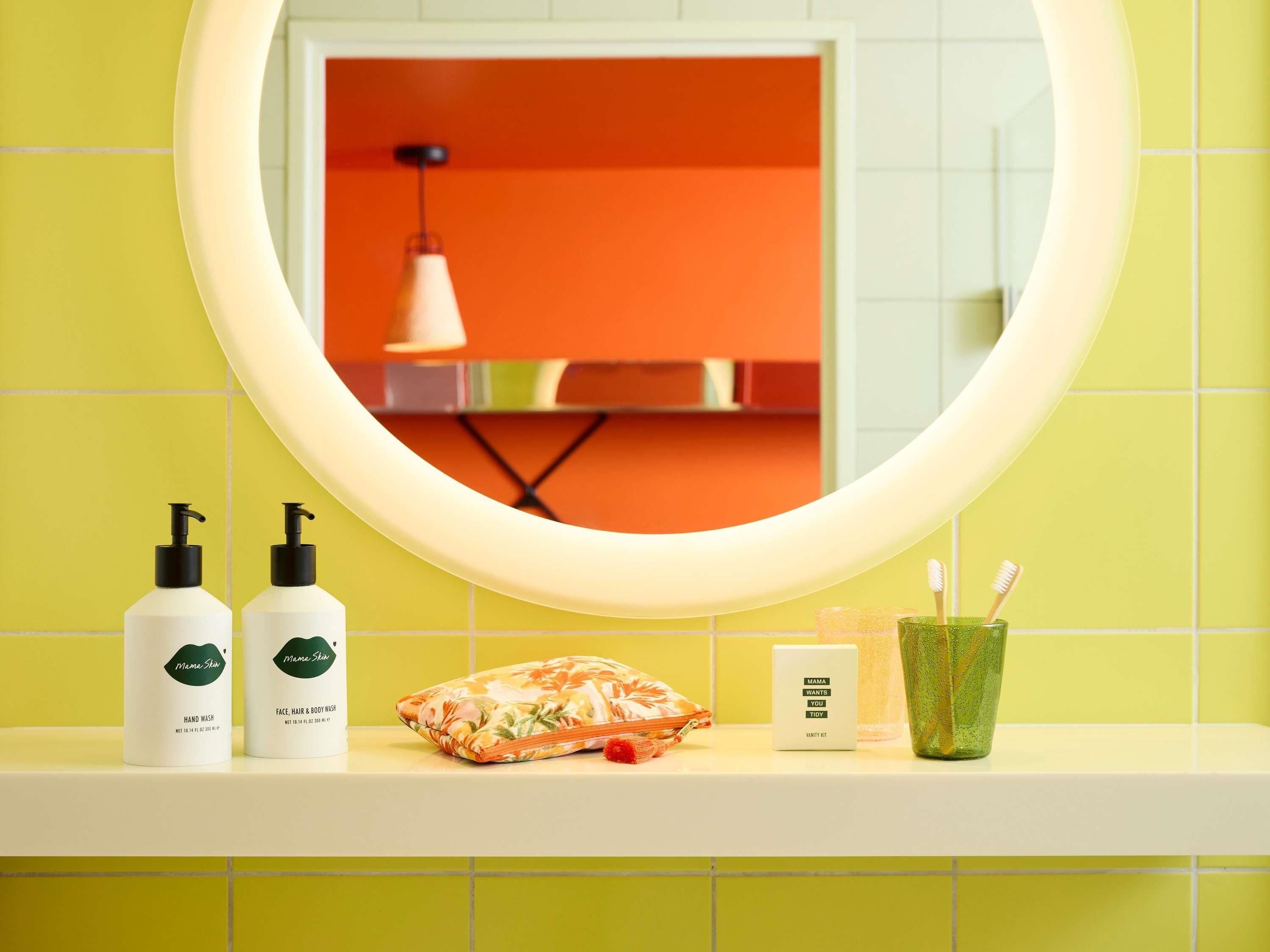 Ein Badezimmer-Waschtisch mit Spiegel, zwei Handseifenflaschen, einem Gesichtsreiniger, einer kleinen Kosmetiktasche, einer Tablett für den Waschtisch und einem Zahnbürstenhalter.