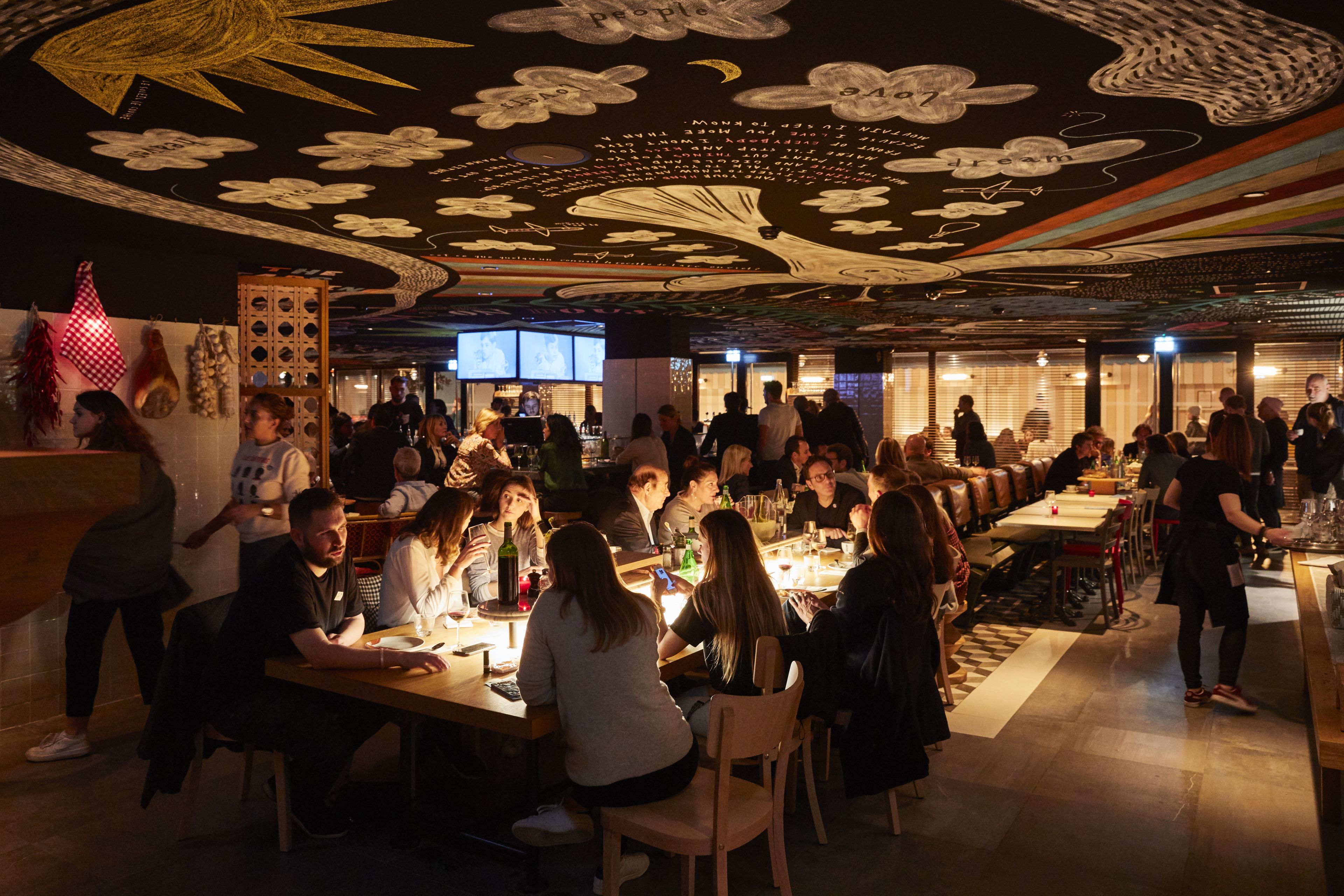 Un restaurante concurrido que destaca por su original diseño de techo, mesas de madera y una zona de bar.