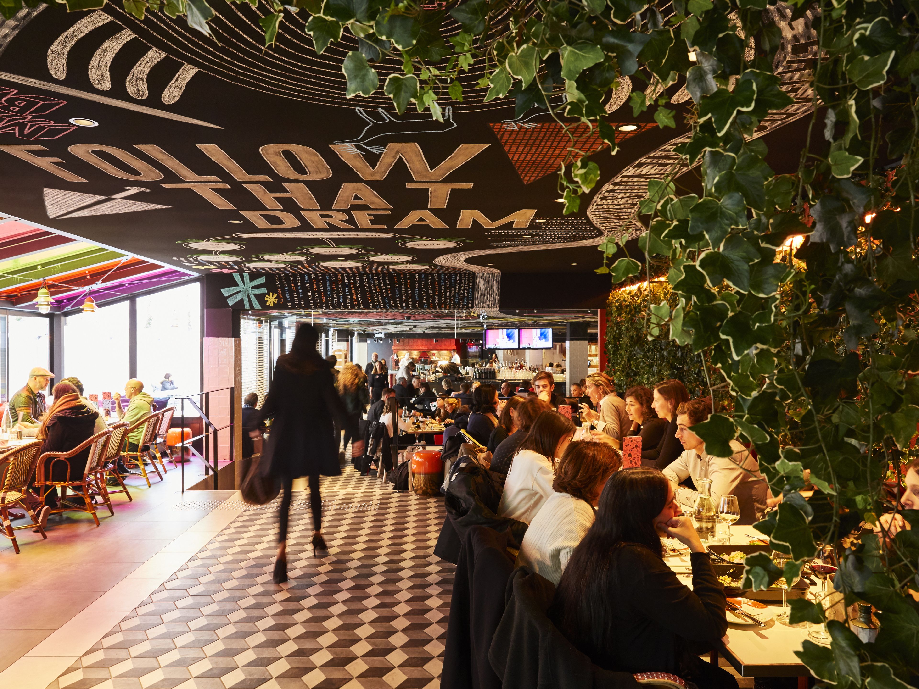A bustling restaurant interior with a checkered floor, a bar area, and a ceiling with a 'Glow Dream' sign.