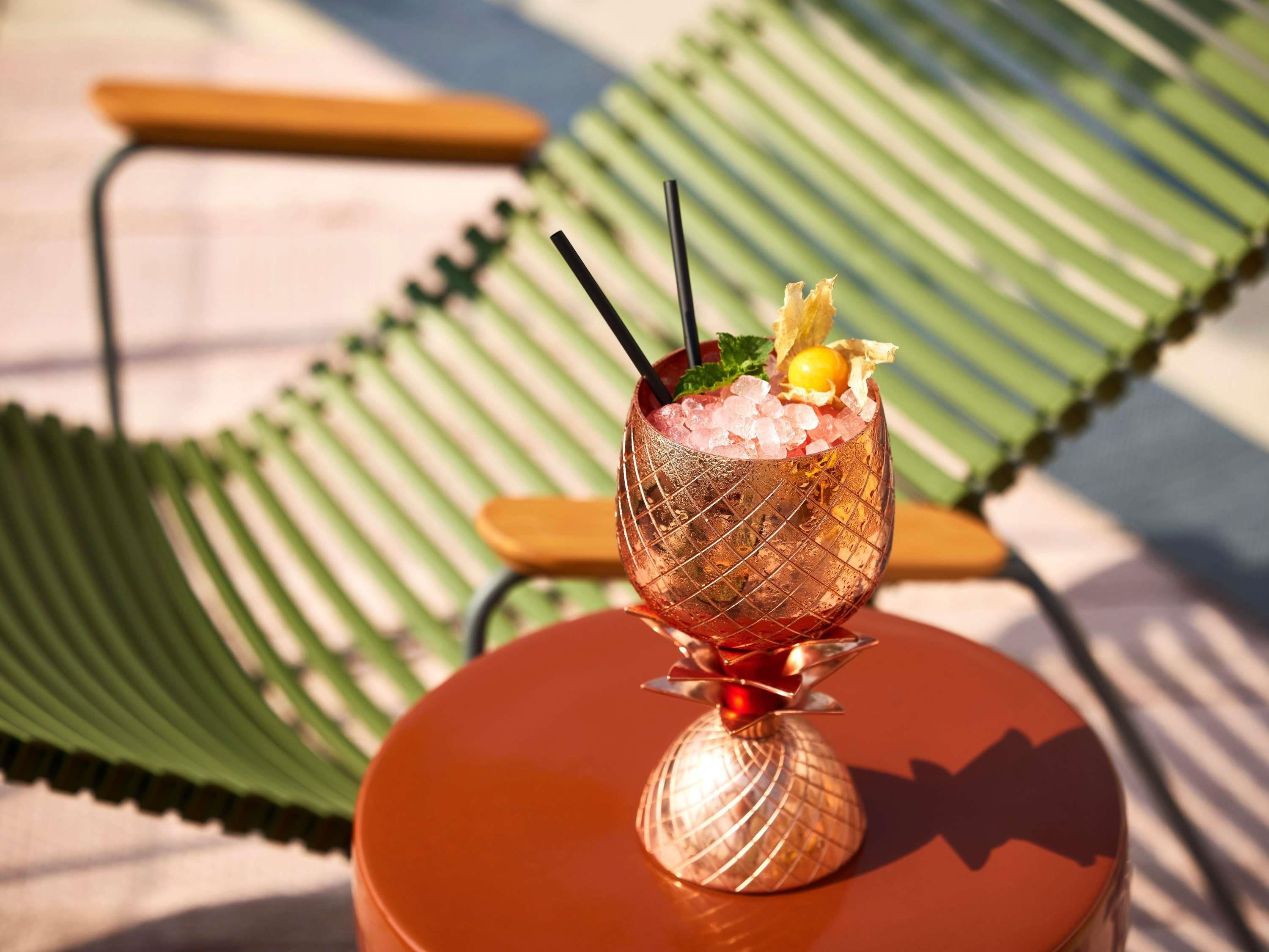 A cocktail in a decorative glass on a table with a green chair in the background.