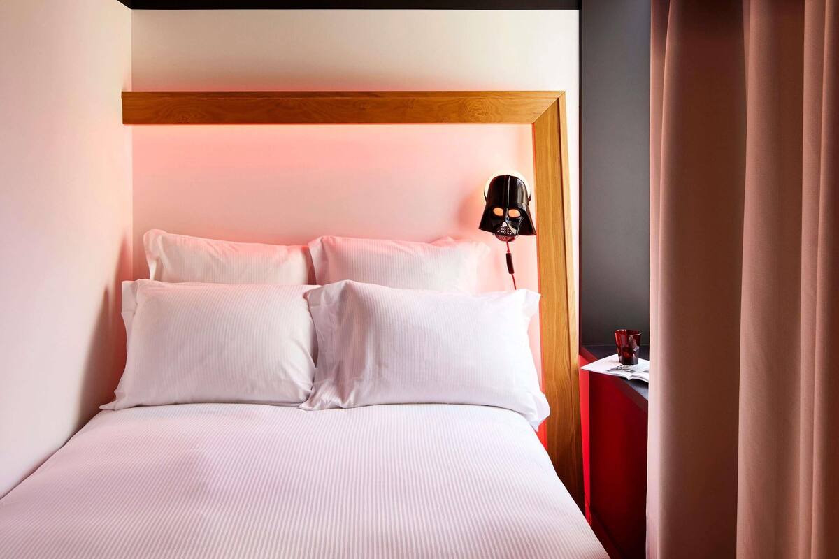 Una habitación de hotel con una cama, una mesita de noche, una lámpara y una cortina.