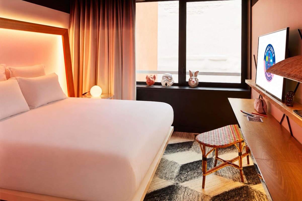 Une chambre d’hôtel avec un lit, un bureau, une chaise, une télévision et une fenêtre avec des rideaux.