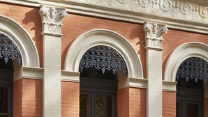 Fachada de edificio con ventanas arqueadas, columnas blancas y un balcón con barandilla.