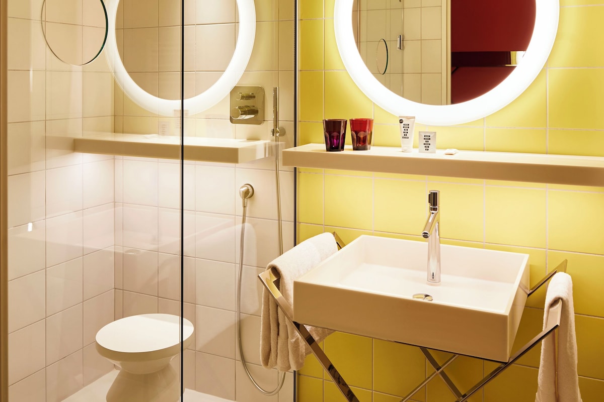 Een moderne badkamer met een douchecabine van glas, een wit wastafelmeubel en een grote spiegel met verlichte randen.
