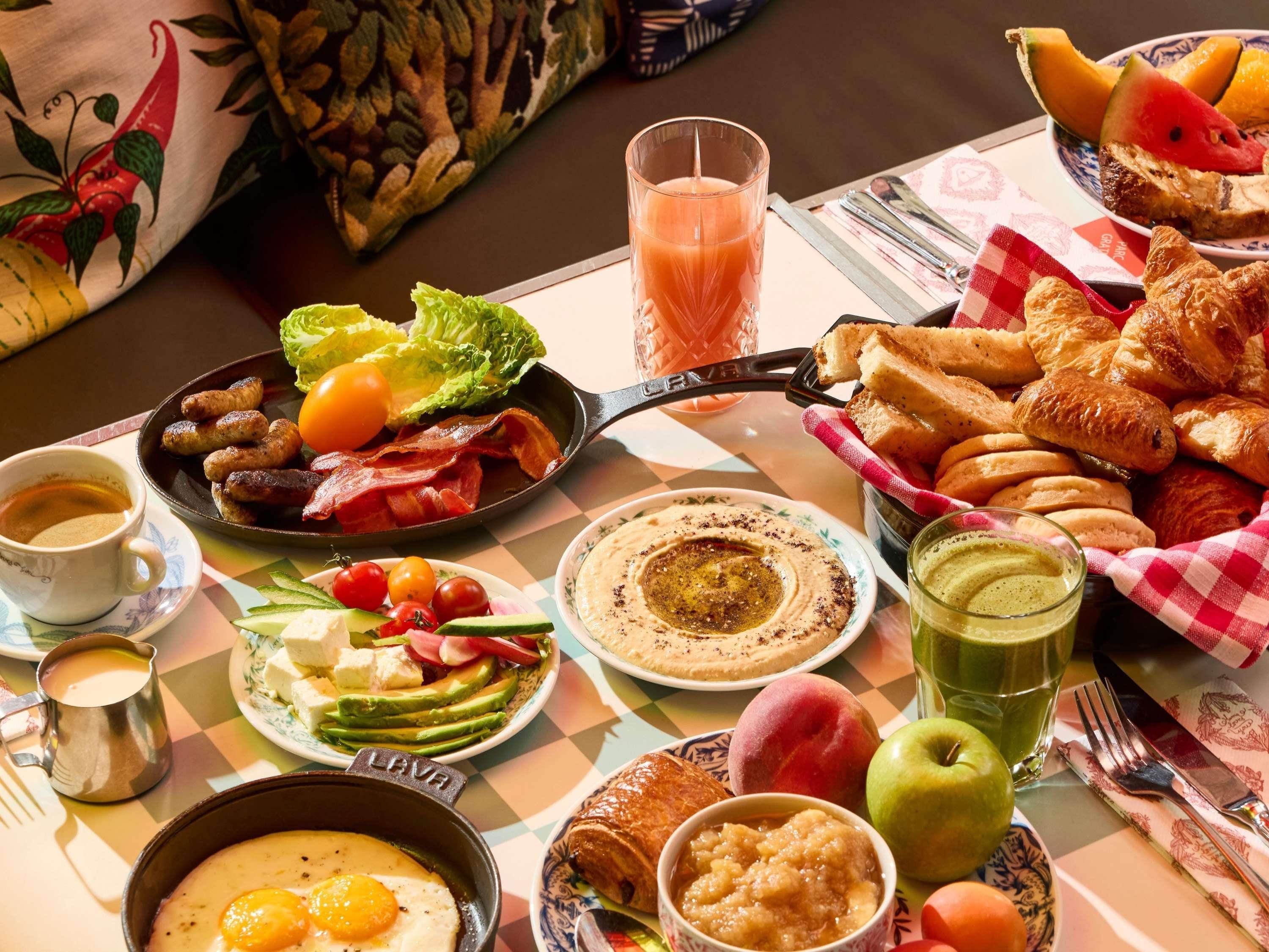 Une table de petit-déjeuner avec divers plats, notamment des œufs, des saucisses, des toasts et des fruits.