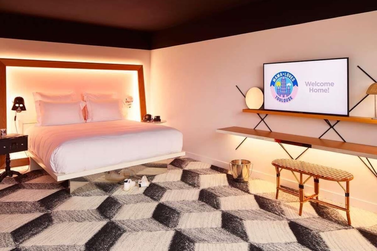 Een moderne hotelkamer met een groot bed, een televisie waarop een welkomstboodschap staat, een kleine tafel en een bank.