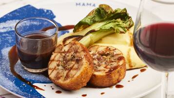 A plate with grilled meat, vegetables, and a glass of red wine on a table with a blue napkin and a patterned placemat.
