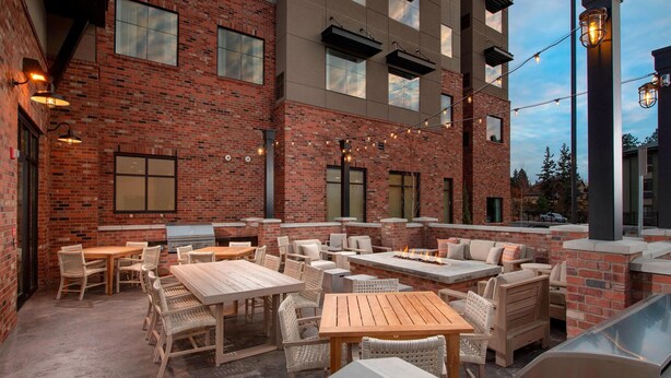 An outdoor patio with brick walls, multiple seating areas, and string lights. - Residence Inn by Marriott Bend (Bend)