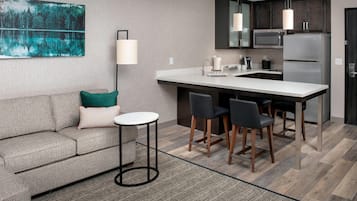 A modern kitchen with a central island, bar stools, a microwave, and a refrigerator.