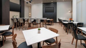 A modern conference room with multiple tables and chairs, a large flat-screen TV mounted on the wall, and a wooden ceiling. - Residence Inn by Marriott Bend (Bend)