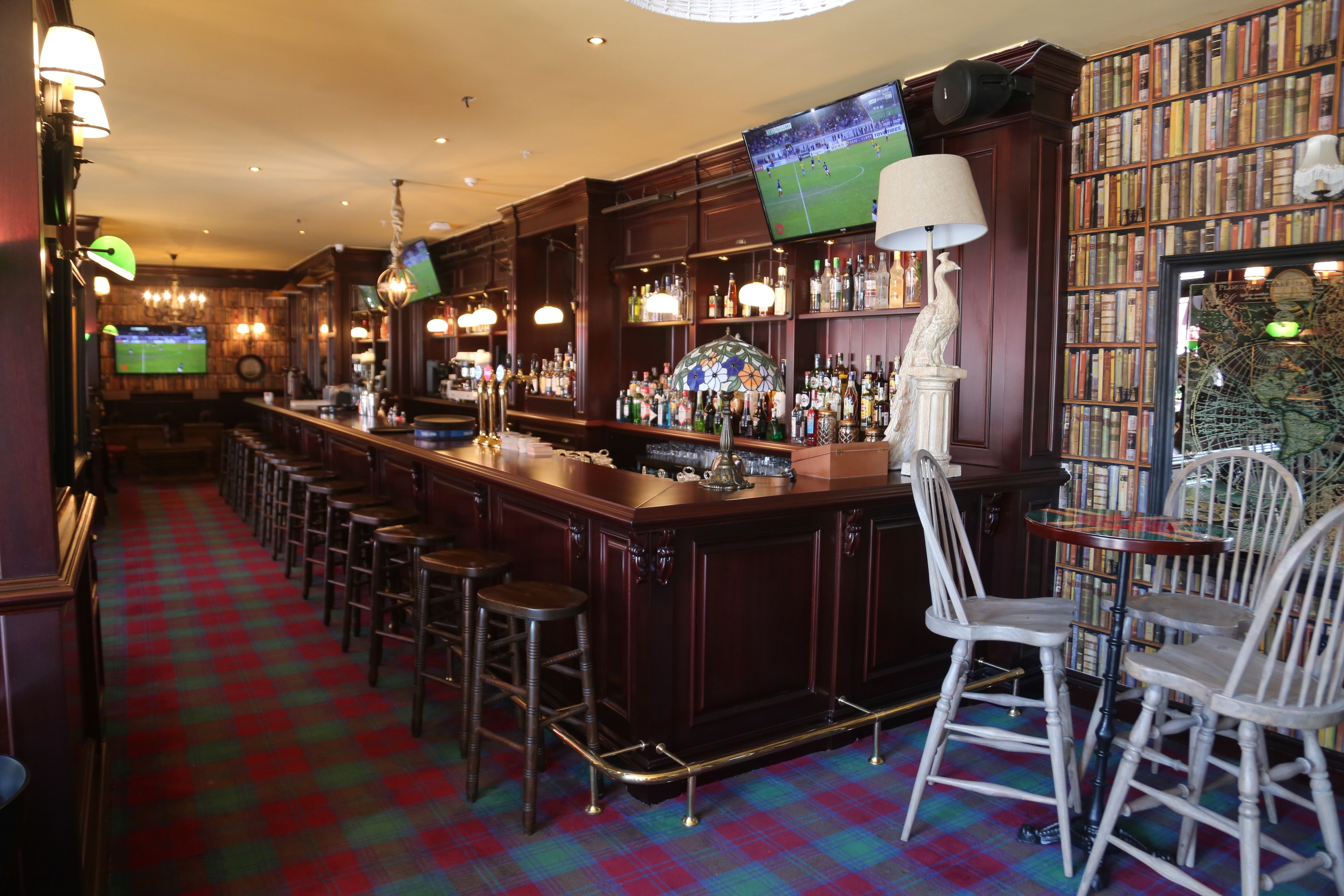 A bar area with a checkered floor, wooden bar counter, stools, and a television screen.