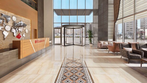 Un moderno vestíbulo de hotel con un mostrador de recepción, alfombra estampada, zona de estar y grandes ventanales que ofrecen vistas de la ciudad.