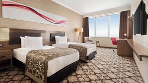 Habitación de hotel con dos camas, un ventanal grande, un escritorio y un televisor.