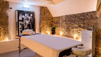Cozy retreat with a bed, bedside table, and chair, set against a rustic stone backdrop.