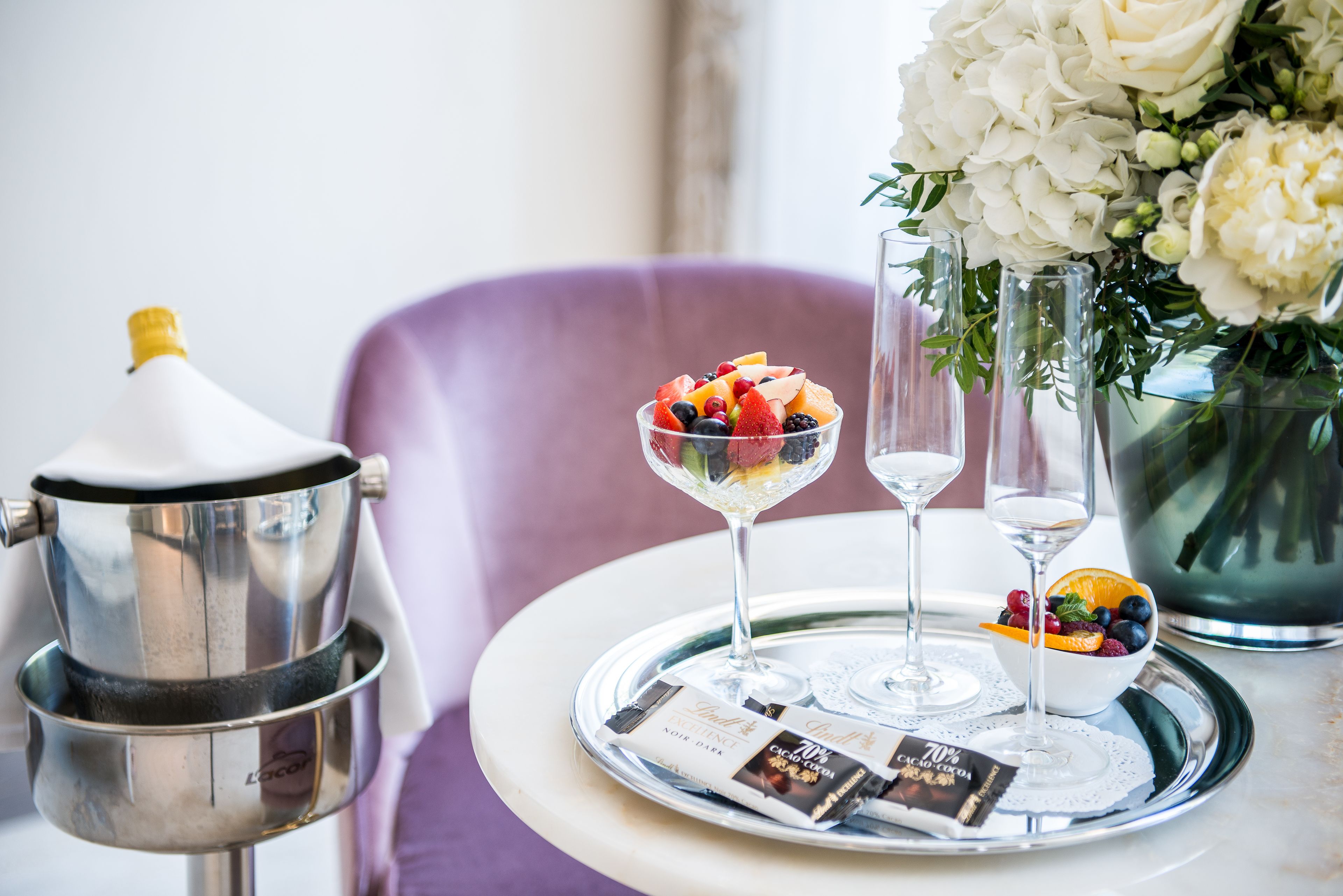 A table with a coffee machine, a glass of fruit, two wine glasses, and a bowl of fruit.