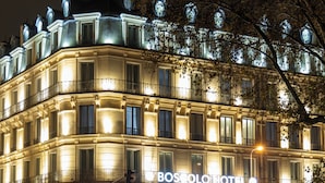 Un hotel de varios pisos con señalización iluminada, balcones y un pavimento mojado y reflectante.