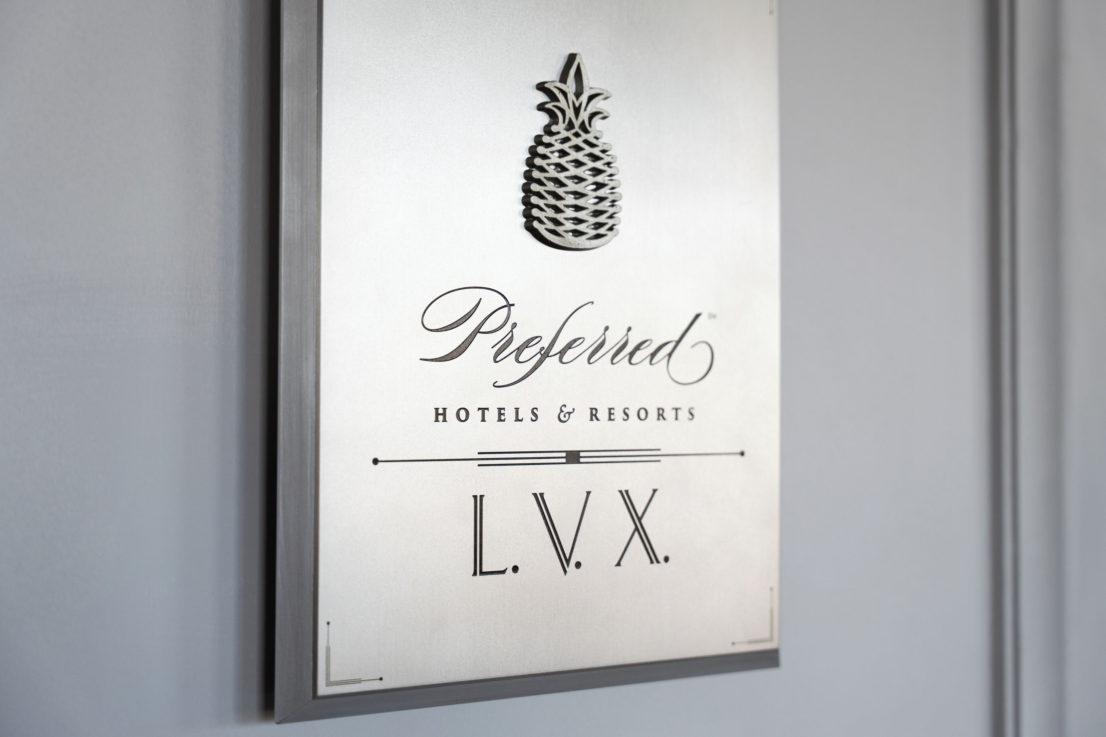 A framed sign with a pineapple logo, the word 'Preferred' in cursive, and 'HOTELS & RESORTS' below it, followed by 'L.V.X.'