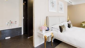 A modern bedroom with a large bed, a vanity with a mirror, and a shower area.