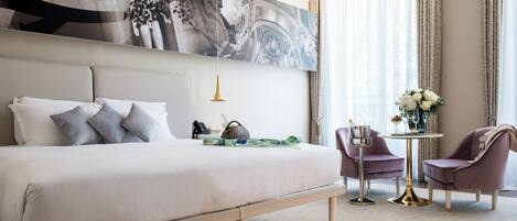 Habitación de hotel con una cama grande, dos sillones, una mesita redonda y un cuadro abstracto de grandes dimensiones en la pared.