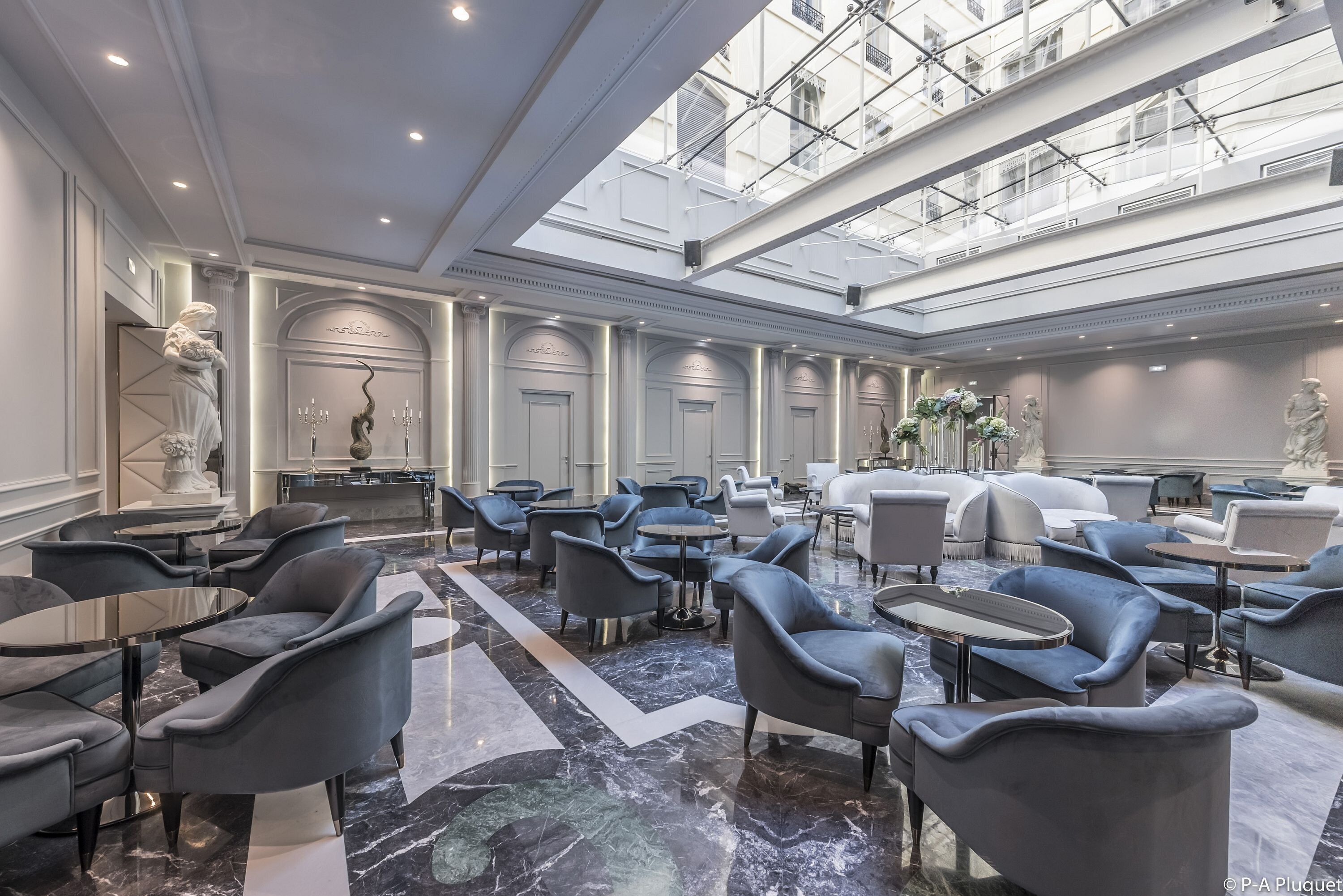 A spacious lobby with marble flooring, modern seating, and a high ceiling with skylights.