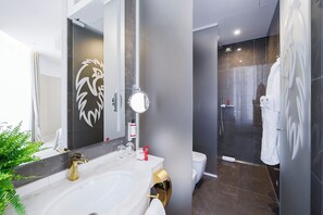 A modern bathroom with a large mirror, a gold faucet, a white sink, and a glass shower enclosure. - Boscolo Lyon Hôtel & Spa (Lyon)