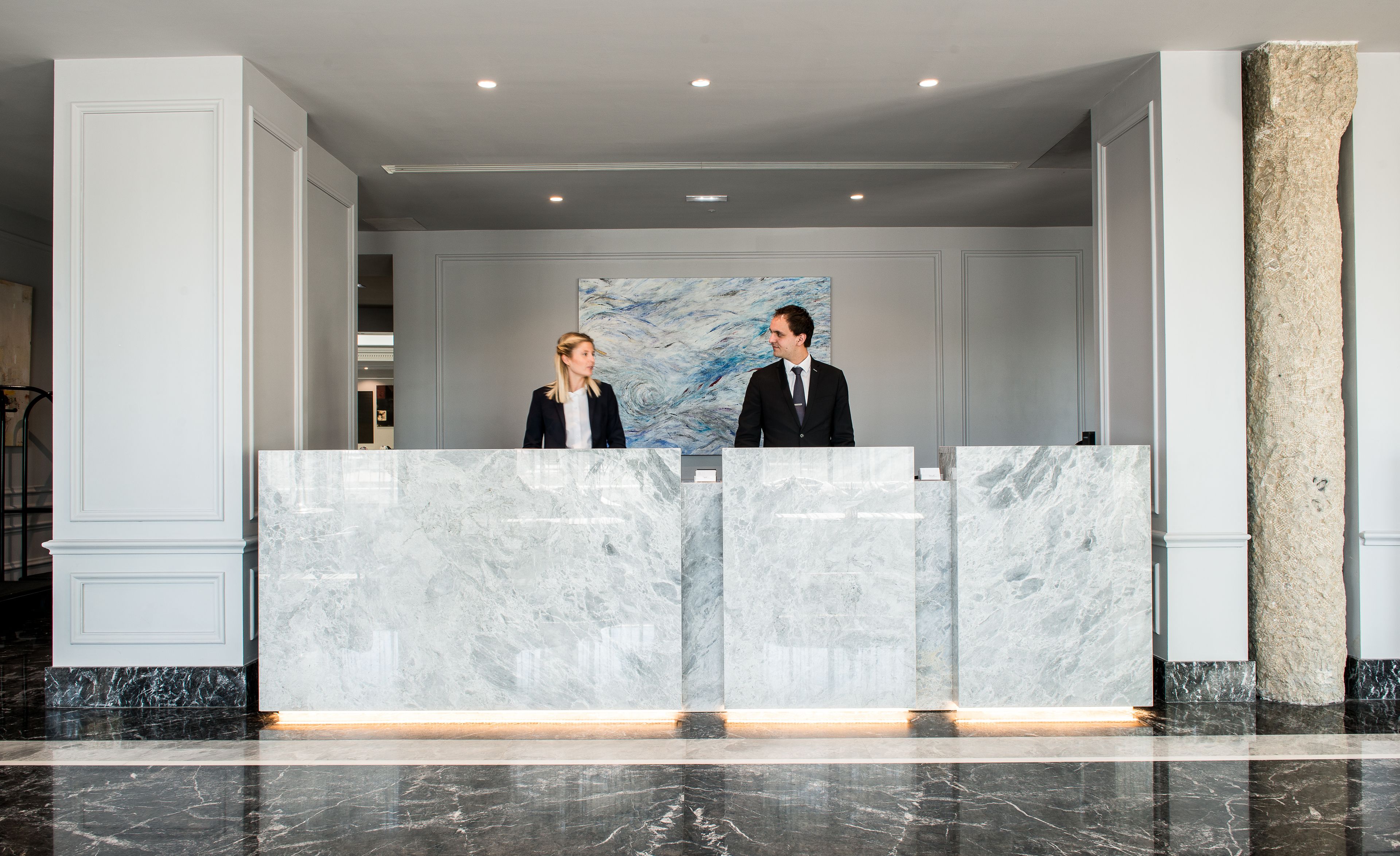 A reception desk with marble panels, a large abstract painting on the wall, and a polished marble floor.