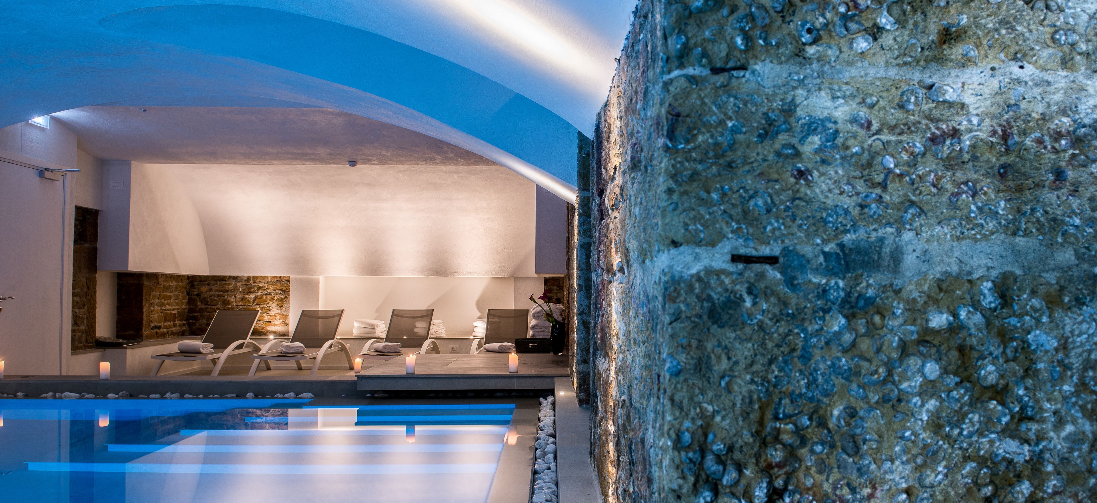 Ein modernes Spa mit Pool, Steinwänden und Liegestühlen.