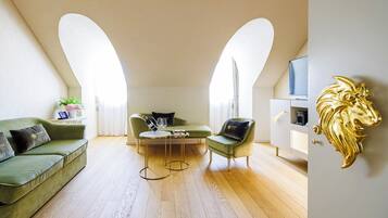 Ett modernt vardagsrum med en grön soffa, en grön fåtölj och ett soffbord. Det finns ett vitt skåp med en tv och en gyllene dekorativ detalj på väggen.