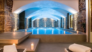 Zona de spa con pared de piedra, piscina y dos áreas de descanso con toallas.