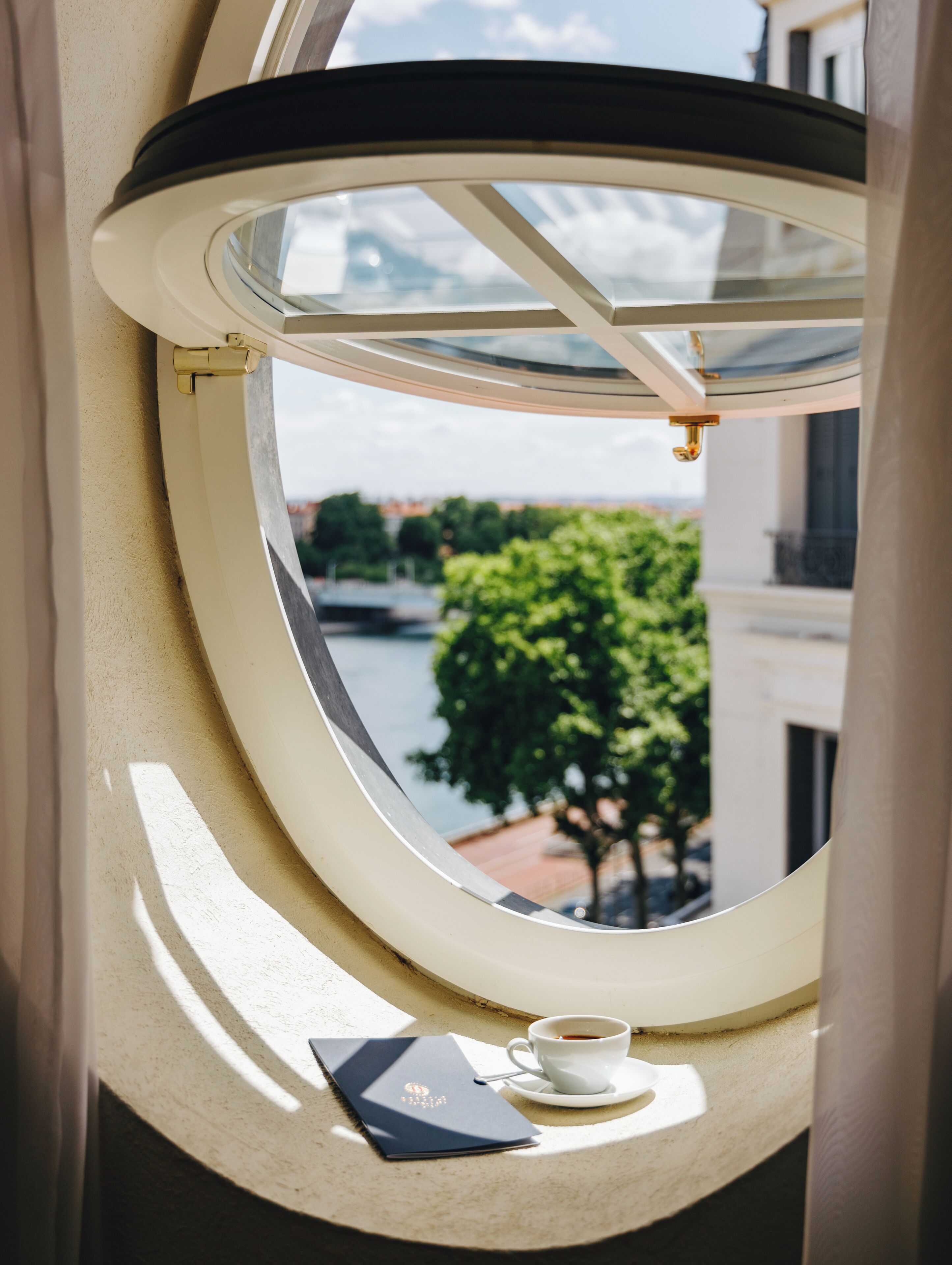 A round window with a view of a tree and a body of water.