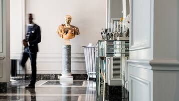 Un hall en marbre orné d’un buste sculpté, une vitrine contenant des objets d’argenterie et une personne qui se promène.