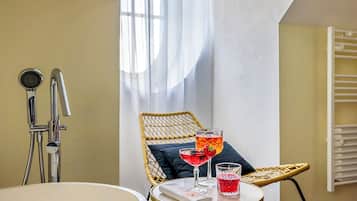 A bathroom with a shower, a sink, and a table with two drinks and a towel.