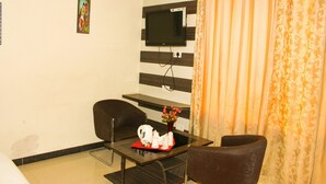 Habitación de hotel con televisor de pantalla plana montado en la pared, una mesita con una bandeja de artículos de tocador, dos sillas y un jarrón decorativo.