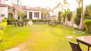 Un patio con césped, un área de descanso y un edificio de techo con tejas y columnas.